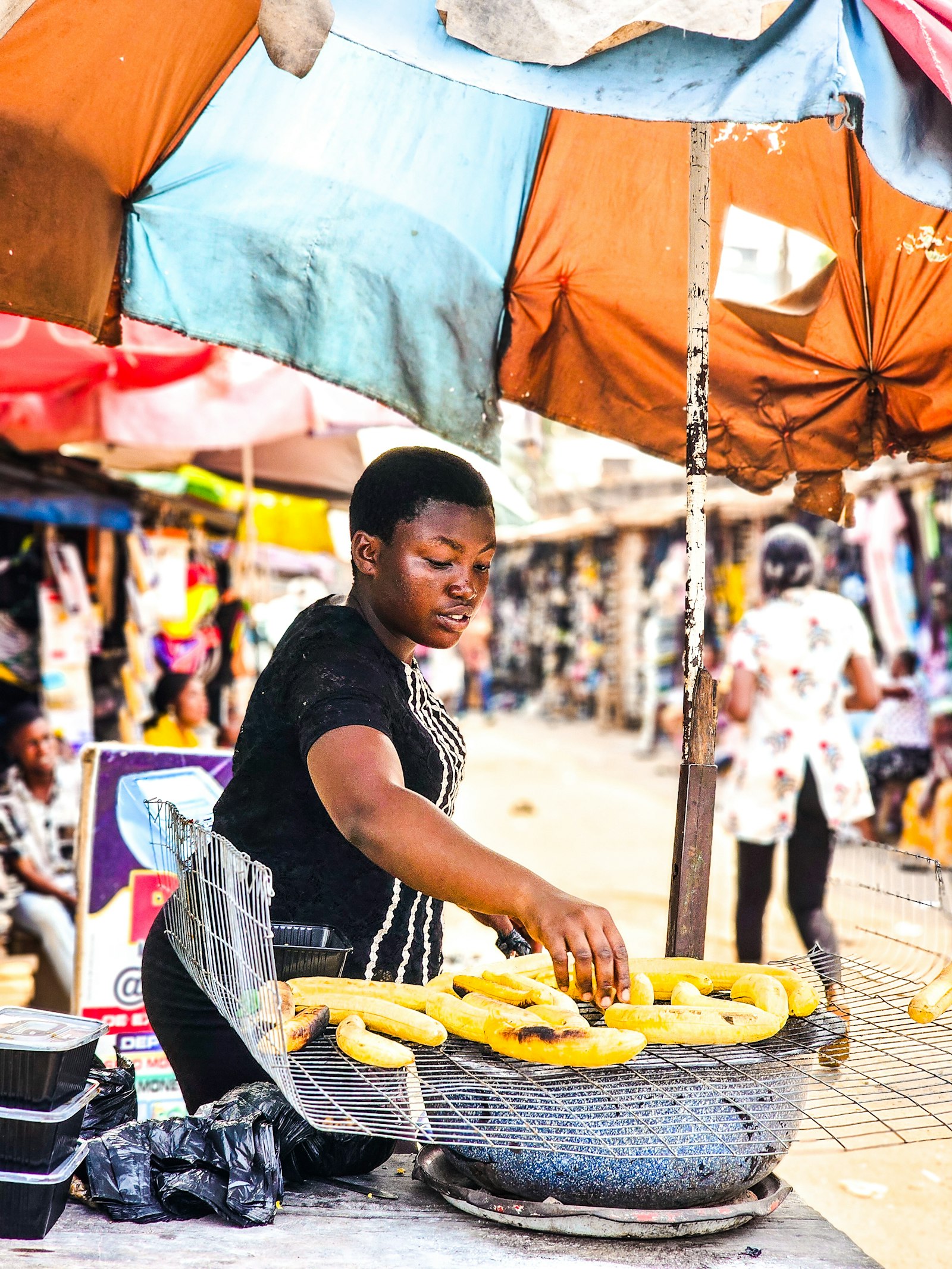 Nigerian market woman roasting plantains at a street stall